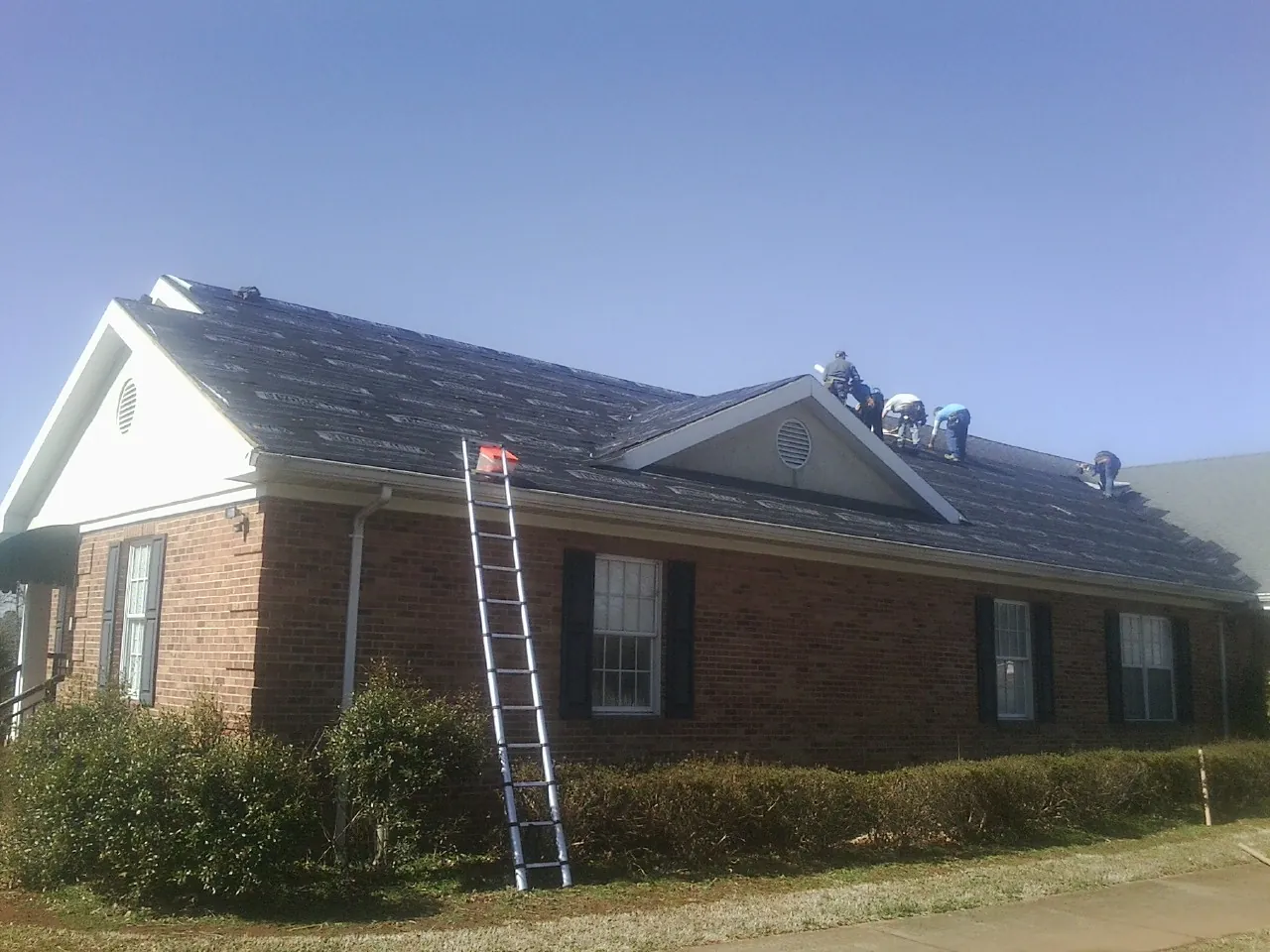 Crew tearing shingles off a brick ranch roof with a ladder set — Metal Roof Repair work by our crew in Hines