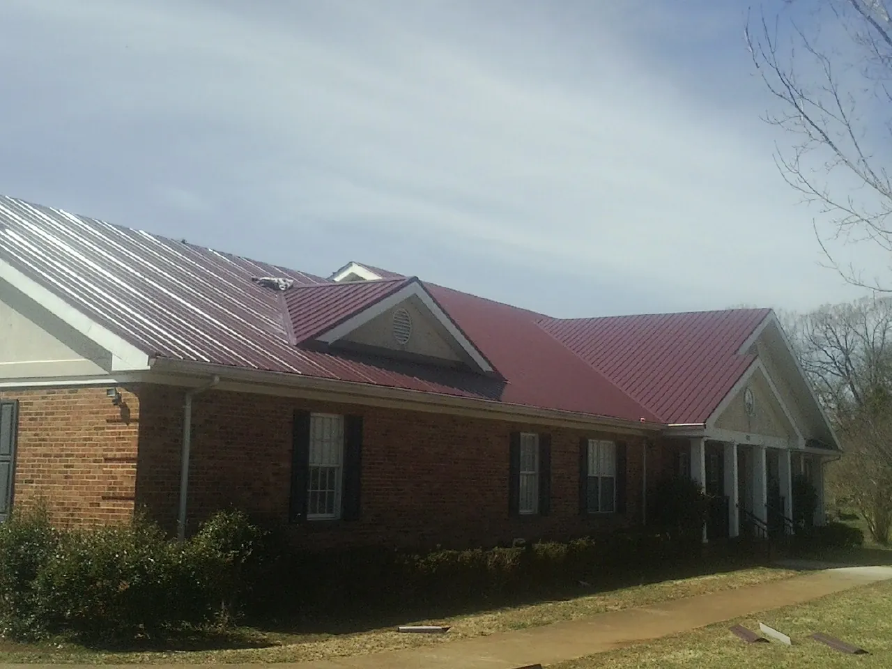 Red metal roof with gabled entries on a long brick building, from a Hail Damage Roof Repair job in Hines
