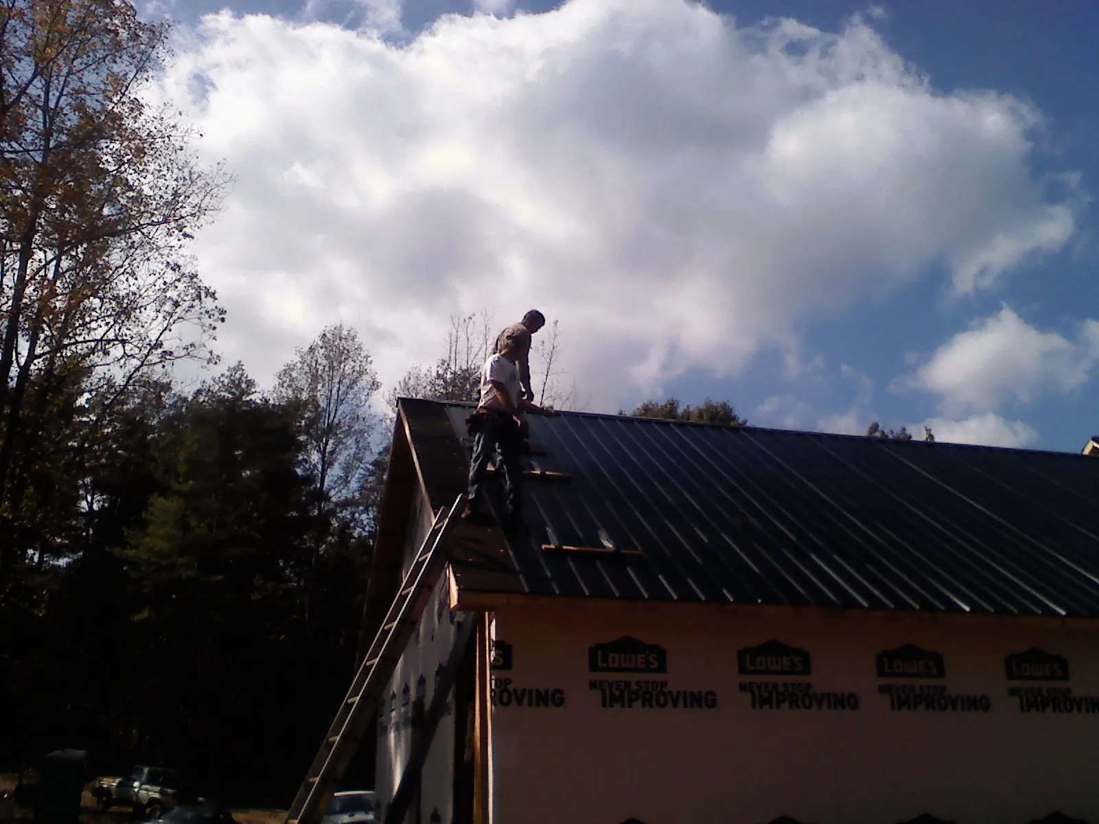 Roofer fastening dark metal panels high against a cloudy sky, from a Roof Inspection job in Hines
